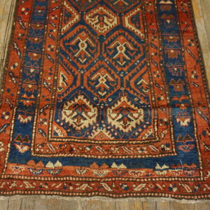 Rust and indigo tribal rug featuring a geometric pattern and borders rests on light, distressed wood flooring.