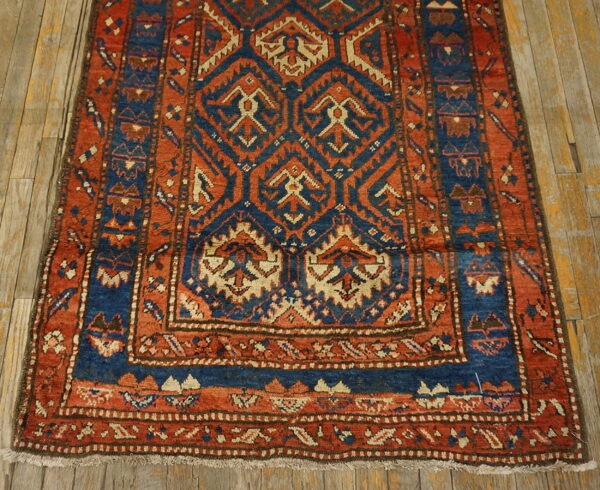 Rust and indigo tribal rug featuring a geometric pattern and borders rests on light, distressed wood flooring.