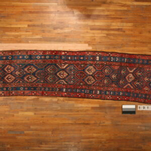 A long runner rug featuring geometric tribal patterns in indigo, red, and cream on a honey hardwood floor.