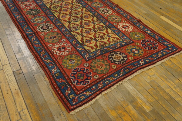 Red, blue, and yellow geometric runner rug with low pile rests on worn, wide plank wood floors.