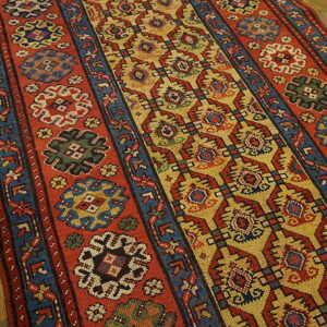 Rust red and mustard yellow runner with tribal geometric patterns sits on rustic hardwood floors.