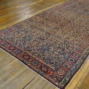 Detailed navy and red low-pile runner rug with all-over floral pattern lies on a distressed wooden floor.