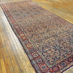 Long low-pile runner with intricate red and navy floral patterns rests on distressed golden wood floorboards.