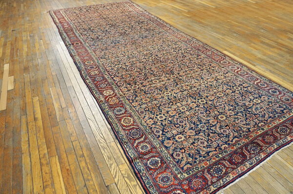 Long low-pile runner with intricate red and navy floral patterns rests on distressed golden wood floorboards.