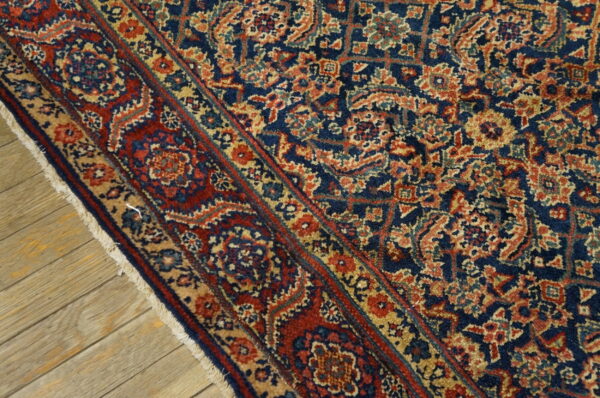 Close-up of a navy blue rug featuring dense, ornate patterns in red, tan, and gold, lying on wood planks.