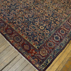 Detail view of a navy blue, red, and beige intricate patterned rug on distressed wooden planks.