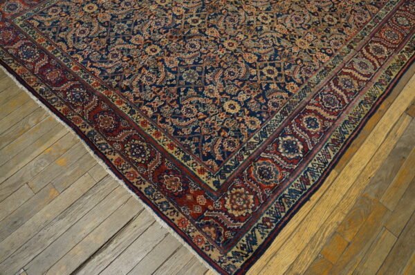 Detail view of a navy blue, red, and beige intricate patterned rug on distressed wooden planks.