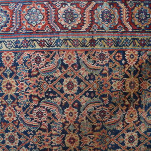 Detailed navy rug with dense red, gold, and light blue geometric floral patterns on concrete flooring.