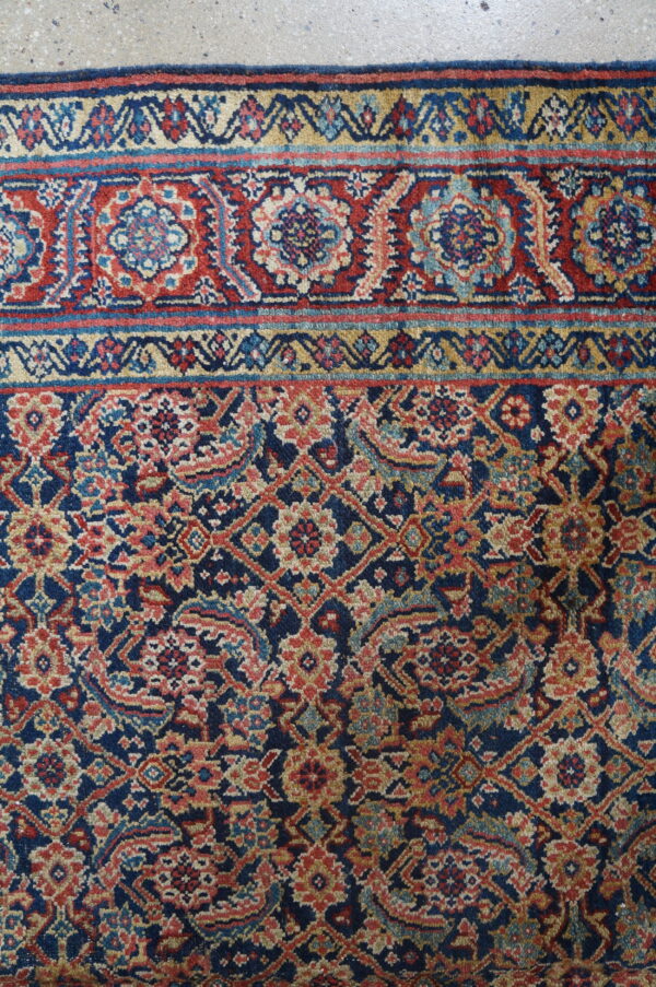 Detailed navy rug with dense red, gold, and light blue geometric floral patterns on concrete flooring.