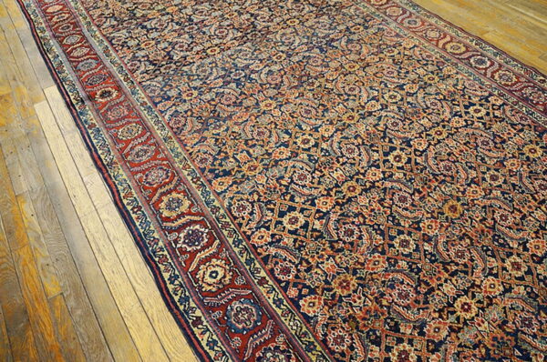 Traditional rug with intricate navy, red, and gold patterns rests on distressed blonde wood floors.