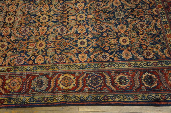 Navy blue, rust, and gold traditional patterned rug detail, showing the border on wood flooring.