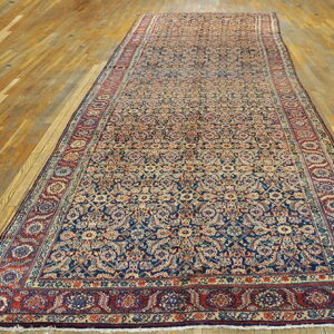 Long runner rug features an intricate navy and tan pattern with wide red floral borders on a wood floor.