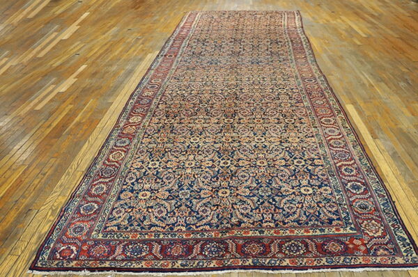 Long runner rug features an intricate navy and tan pattern with wide red floral borders on a wood floor.