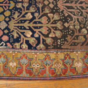 Close-up of a low-pile rug with stylized floral motifs in navy, red, and gold, bordering an ornate star pattern on wood floor.