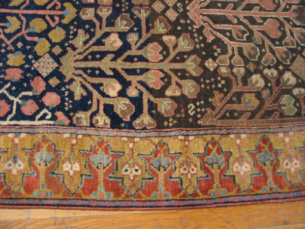 Close-up of a low-pile rug with stylized floral motifs in navy, red, and gold, bordering an ornate star pattern on wood floor.
