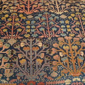 Low-pile rug detail showing horizontal bands of coral pink and gold stylized trees on indigo blue.