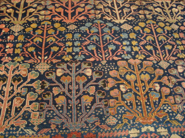 Low-pile rug detail showing horizontal bands of coral pink and gold stylized trees on indigo blue.