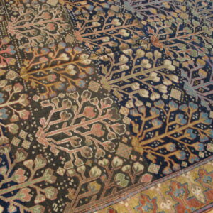 Multi-colored rug with botanical designs and a prominent geometric gold and red border on a wooden floor.