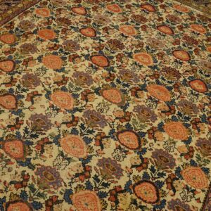 Ornate floral rug with a cream field, large coral flowers, and a dark blue border on wood floors.