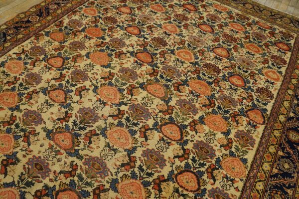 Ornate floral rug with a cream field, large coral flowers, and a dark blue border on wood floors.