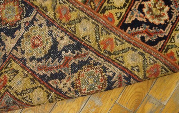 Close-up showing the reverse of a tightly woven, low-pile traditional rug on golden wood flooring.