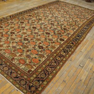 A large low-pile rug featuring a multicolored floral pattern on a cream field and a dark navy border, laid on wooden planks.