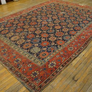 Multicolored floral rug with a dark blue field and wide red border rests on aged yellow wood plank flooring.
