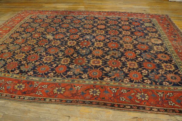 Navy blue and terracotta red floral pattern rug, showing wear, displayed on wide plank wood flooring.