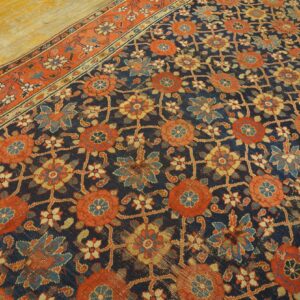 Distressed navy rug with orange and blue floral pattern and rust border shown on worn hardwood floors.