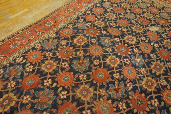 Distressed navy rug with orange and blue floral pattern and rust border shown on worn hardwood floors.