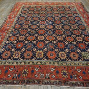 Navy floral pattern rug with a vibrant rust border sits on weathered light-colored wood flooring.