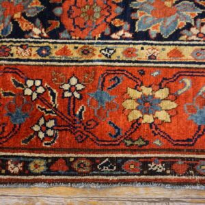 Traditional patterned rug with deep red and navy borders, featuring floral designs on distressed floorboards.