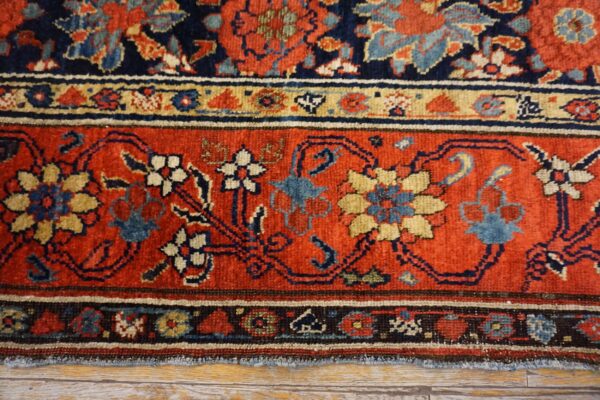 Traditional patterned rug with deep red and navy borders, featuring floral designs on distressed floorboards.