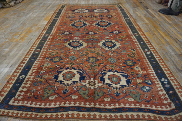 Terracotta and navy blue patterned rug with multiple geometric borders displayed on worn wood planks.