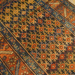 Angled view of a rust, navy, and gold geometric rug lying on light wood planks.