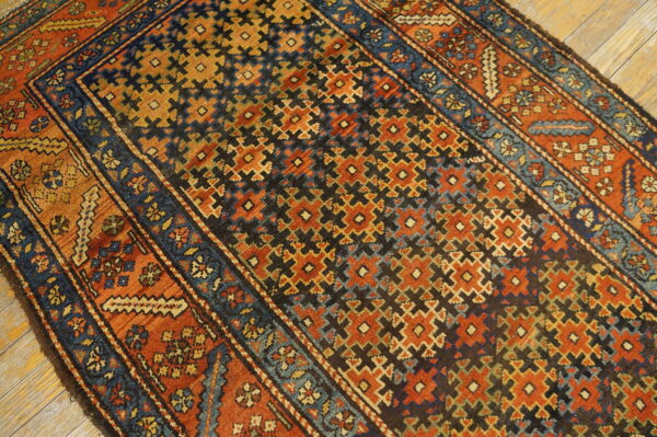 Angled view of a rust, navy, and gold geometric rug lying on light wood planks.