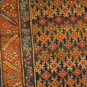 Geometric and floral patterned rug in rust, blue, and dark colors resting on wood flooring.