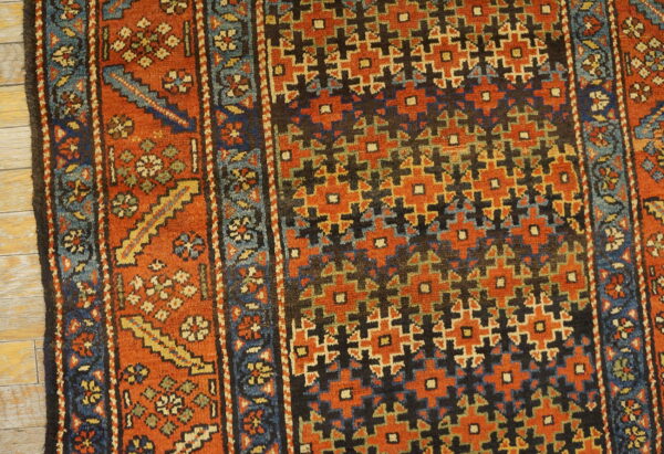 Geometric and floral patterned rug in rust, blue, and dark colors resting on wood flooring.
