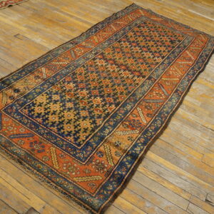 Navy and orange geometric rug with a detailed border placed on worn blonde wood flooring.