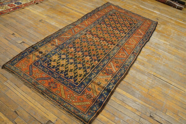 Navy and orange geometric rug with a detailed border placed on worn blonde wood flooring.