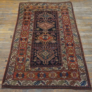 Geometric rug in navy, red, gold, and cream colors lies centered on worn plank wood flooring.