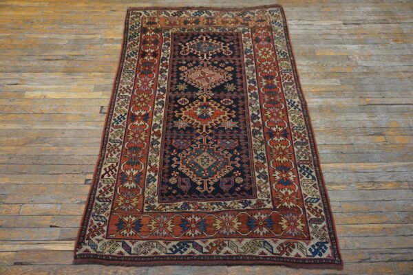 Geometric rug in navy, red, gold, and cream colors lies centered on worn plank wood flooring.