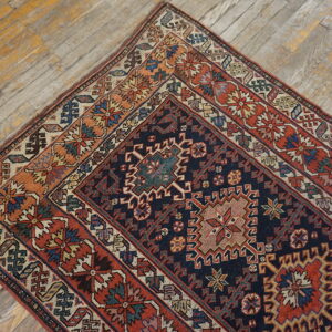 A richly detailed navy and rust geometric rug lies diagonally on rustic, faded wood plank floors.