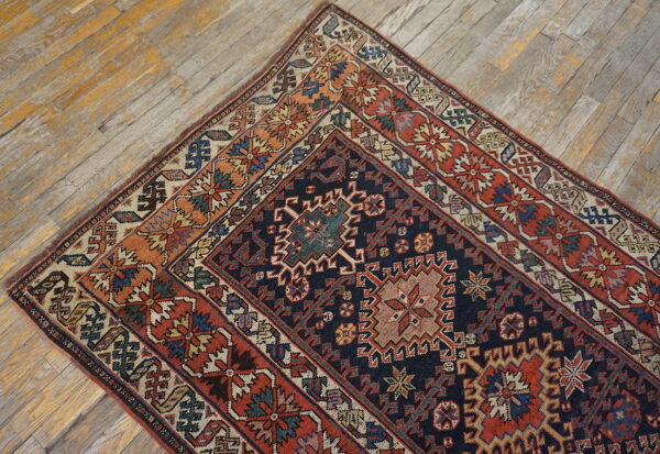 A richly detailed navy and rust geometric rug lies diagonally on rustic, faded wood plank floors.