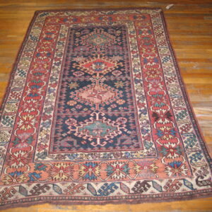 Dark blue, red, and beige traditional geometric rug displayed on rustic honey-colored wood planks.