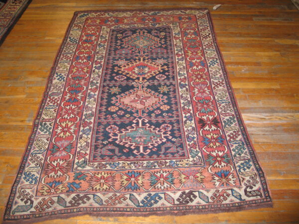 Dark blue, red, and beige traditional geometric rug displayed on rustic honey-colored wood planks.