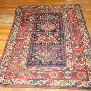 Traditional navy, rust, and beige geometric rug with elaborate borders is centered on hardwood flooring.