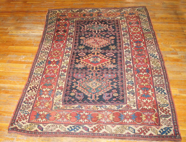 Traditional navy, rust, and beige geometric rug with elaborate borders is centered on hardwood flooring.