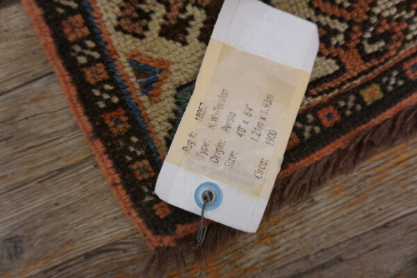 A detail shot of a rust, cream, and dark patterned rug with fringe on rustic wood planks.