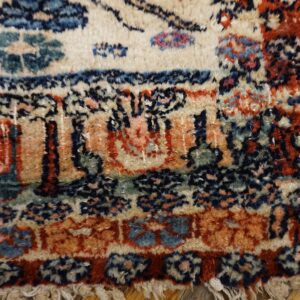 Detailed view of a shaggy rug border with red, blue, cream, and green traditional motifs over wood planks.